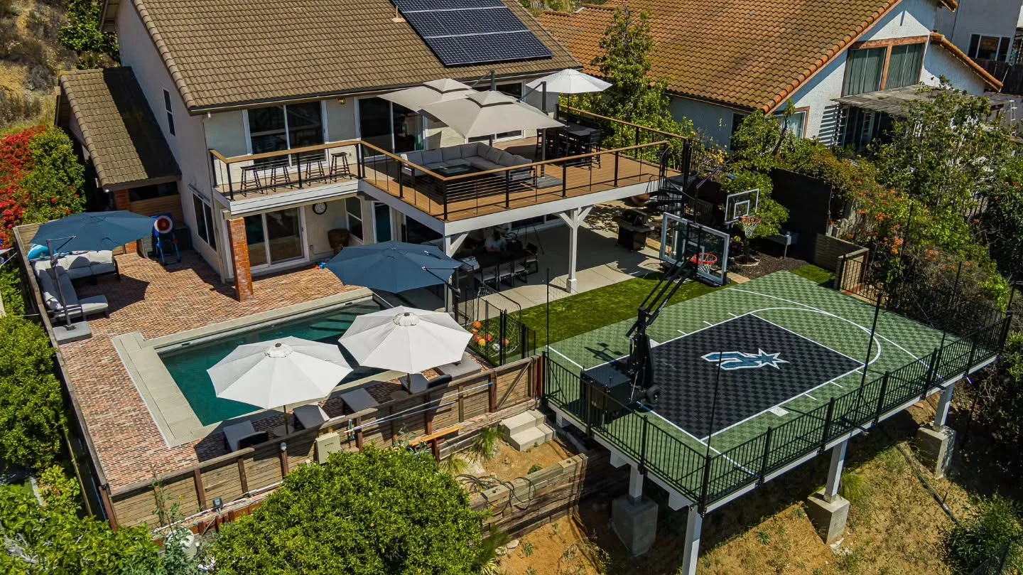 Multi-level composite deck with metal railings, patio covers, and sports court from aerial view