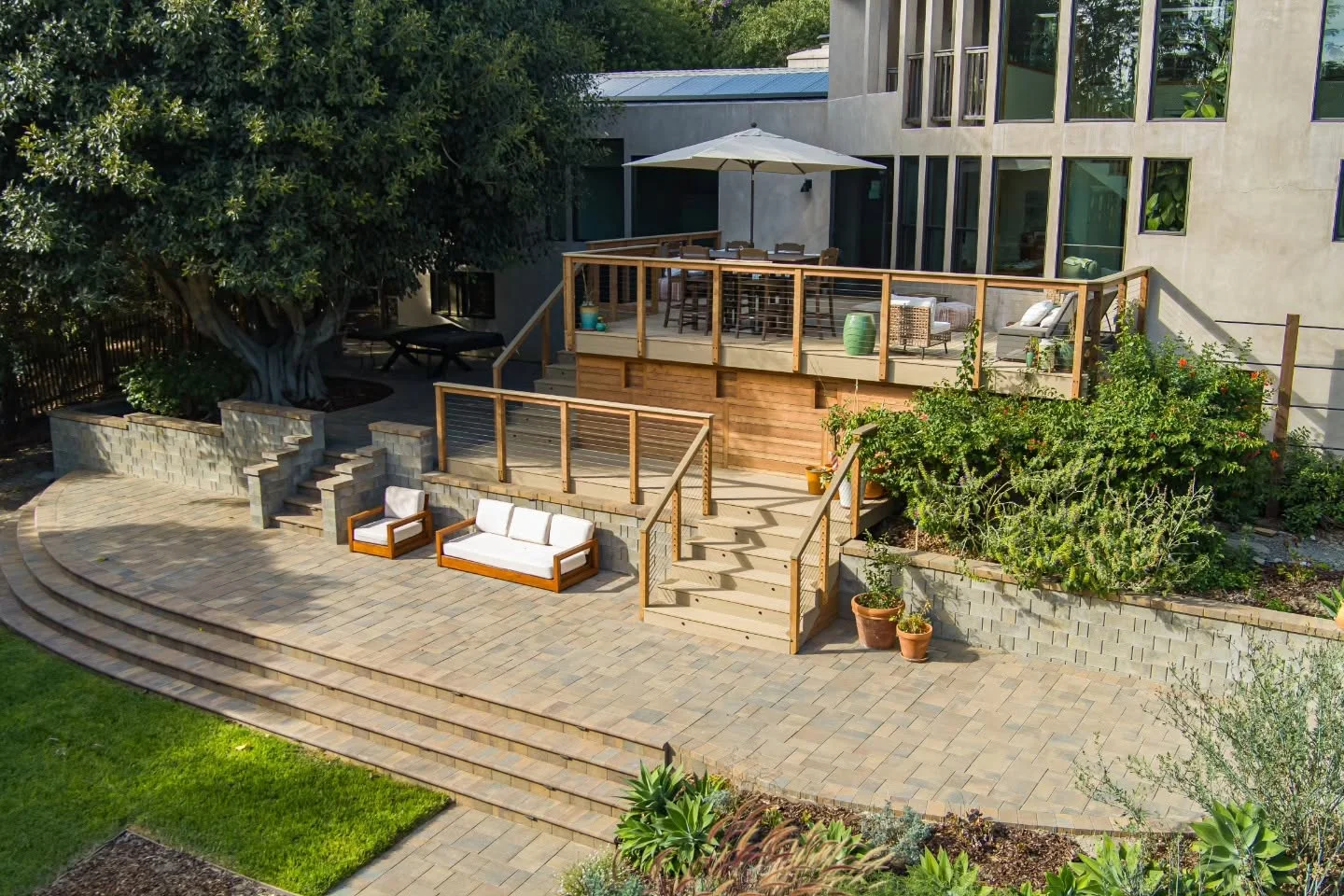 Two-level wooden deck with cable railings, curved paver patio, and stone seating walls