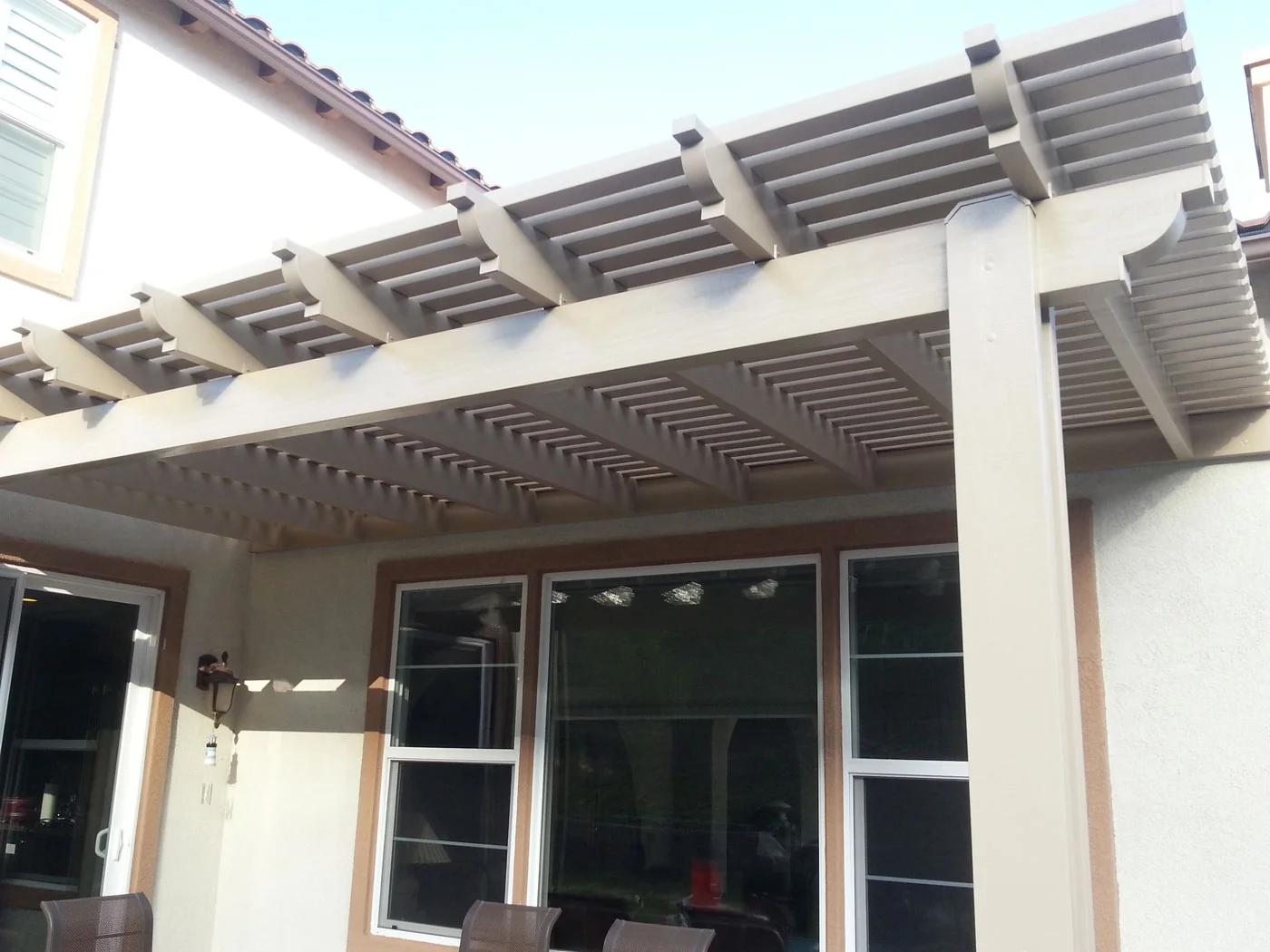 Gray and white alumawood patio cover with lattice beams over residential patio with glass doors