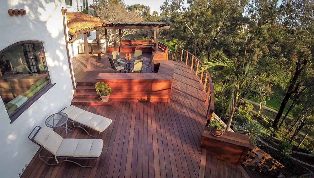 Multi-level hardwood deck with pergola, lounge chairs, and planter boxes surrounded by trees