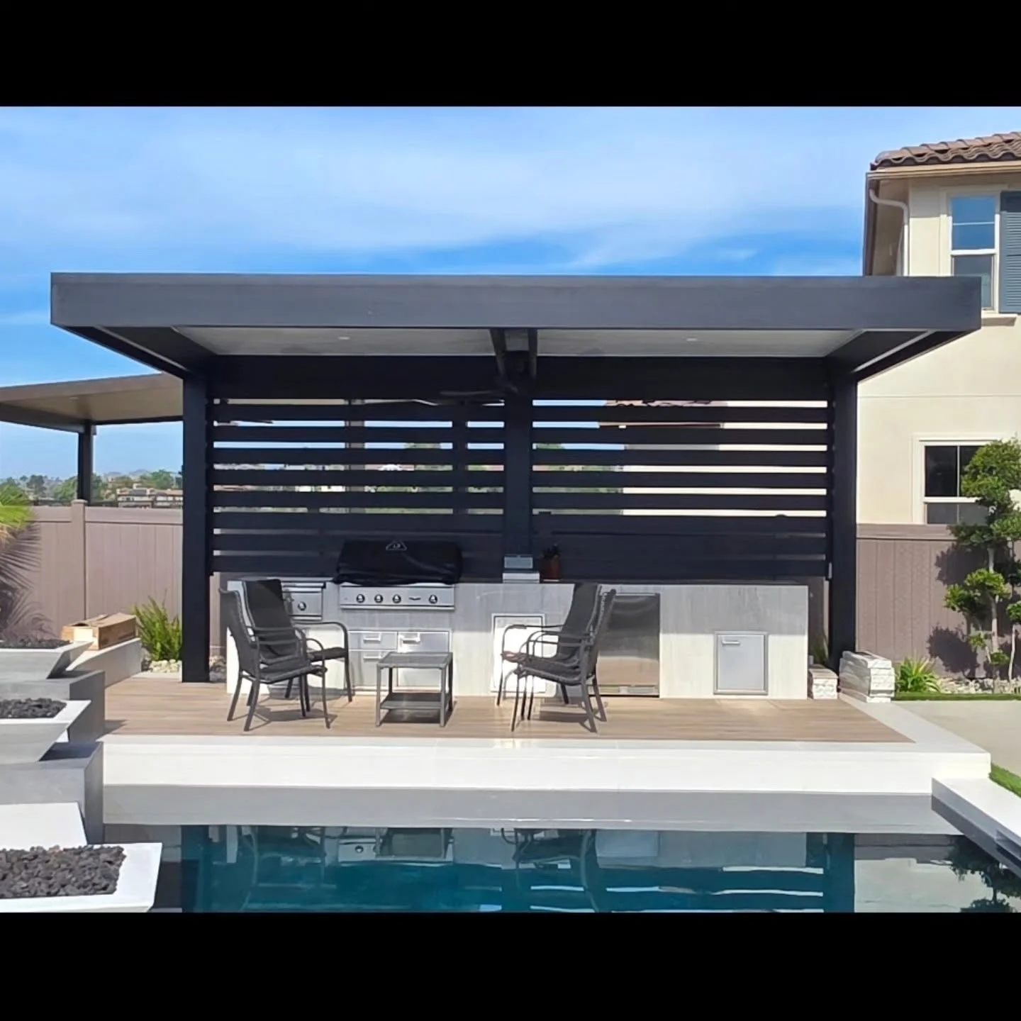 Black aluminum pergola with louvered panels over composite deck and stainless steel outdoor kitchen