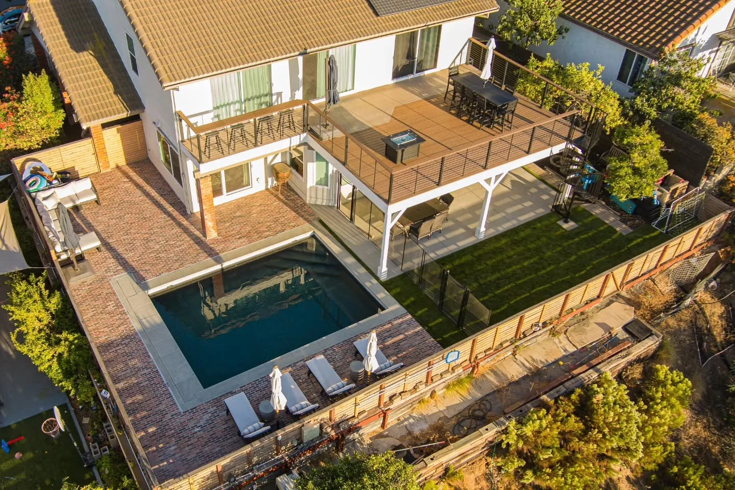 Aerial view of multi-level composite and paver deck with pool, white pergola, and cable railings
