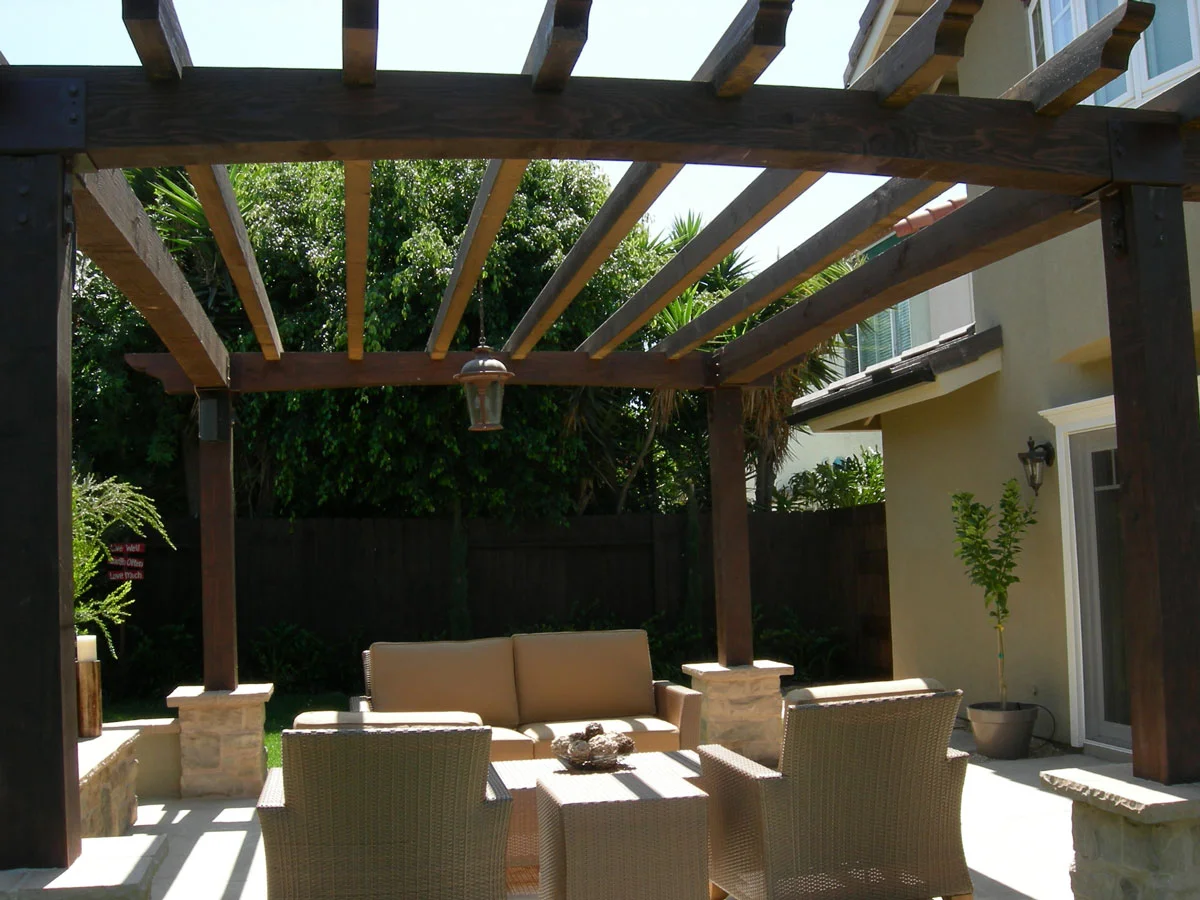 Stained wood pergola with curved brackets over patio seating area with stone planters