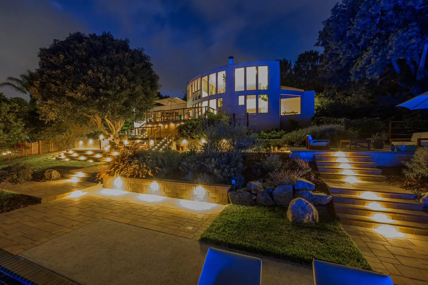 Multi-level composite deck with LED lighting, wooden steps, and illuminated paver pathways