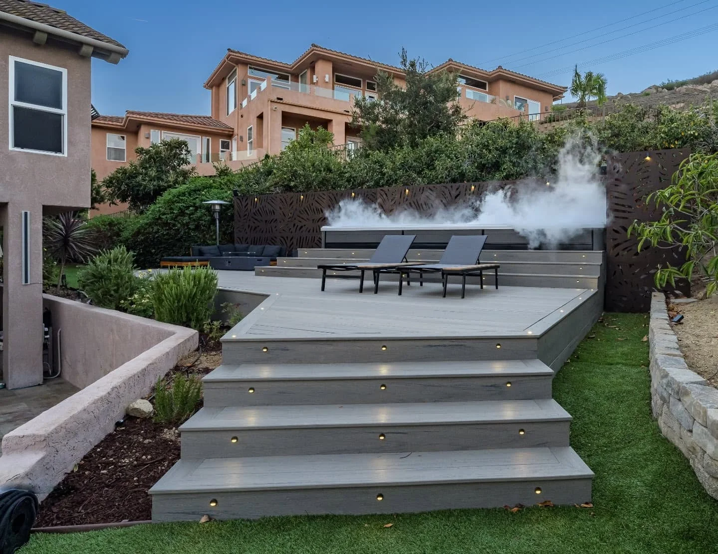 Gray composite deck with brass lighting, built-in benches, spa, and metal privacy screens