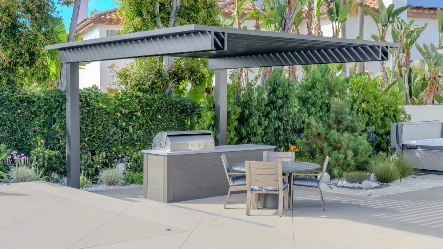 Black aluminum pergola with louvered roof over outdoor kitchen island and dining area