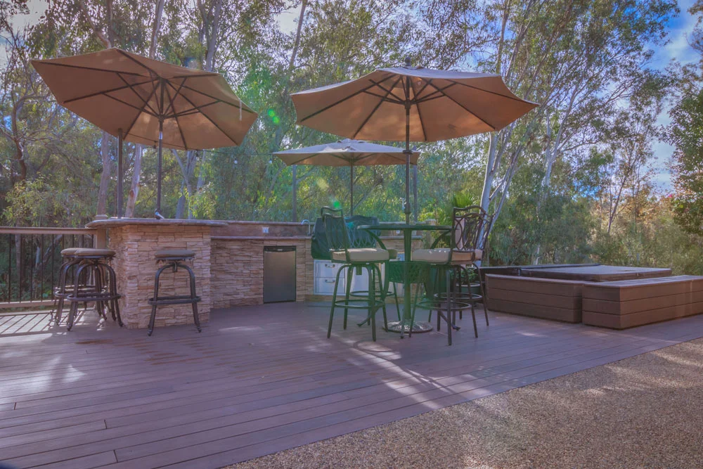 Composite deck with brick bar, umbrellas, spa surround, and integrated seating among trees