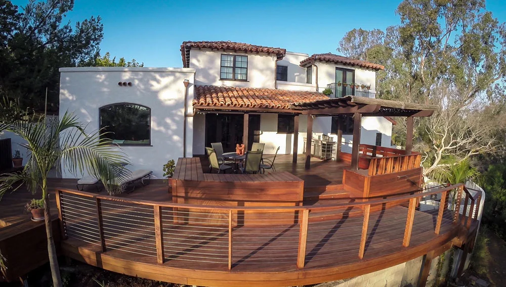 Large curved hardwood deck with metal railing and attached pergola over patio seating area