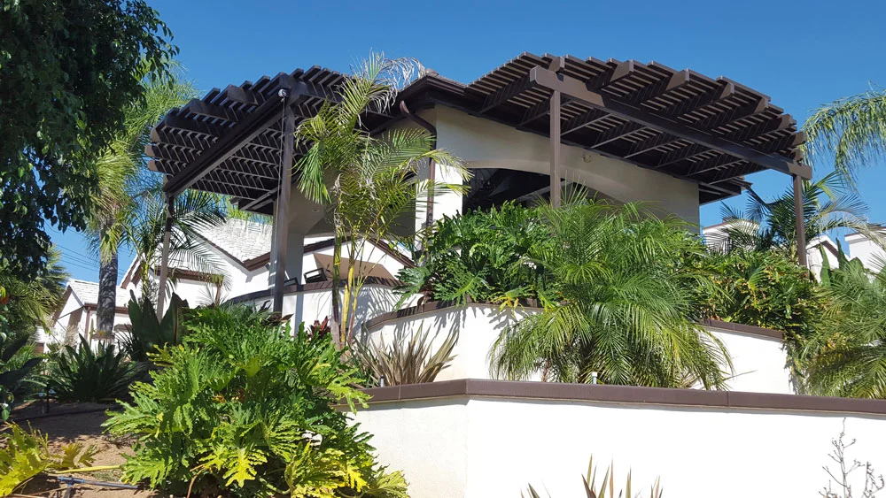 Dark wood pergola with lattice panels over white stucco patio, tropical plants and palms