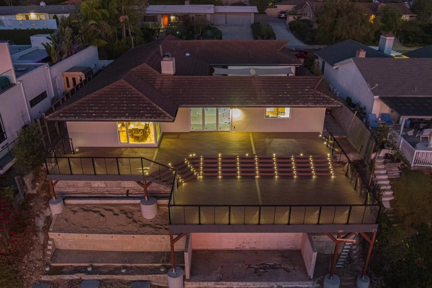 Aerial view of illuminated composite deck with LED lighting, metal railings, and attached patio cover at dusk