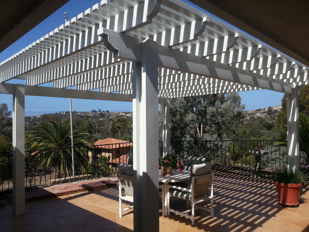 White aluminum pergola with slatted roof over patio with wrought iron railing and hillside views